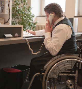 Ein Mann sitzt im Rollstuhl an einer Hotelrezeption.