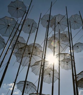 Sonniger Himmel, oben an Stangen sind viele Regenschirme befestigt. Symbol für Rettungsschirm.