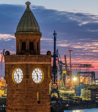 Uhrturm der St. Pauli Landungsbrücken an der Elbe. Im Hintergrund Hafenanlagen. Warmes Abendlicht.
